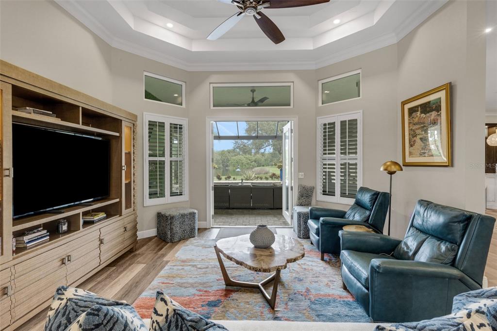 A living room with a tray ceiling, wood-look flooring, and an open view to the kitchen — 7732 DONALD ROSS ROAD W, SARASOTA, FL