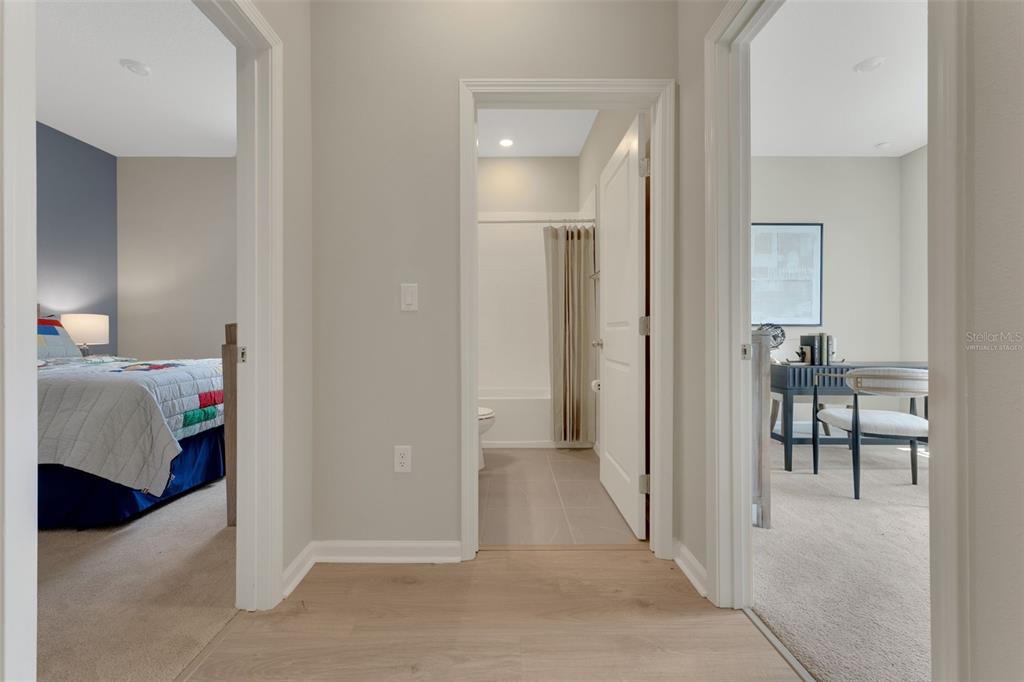 A hallway with light wood flooring leads to a bathroom flanked by two bedrooms — 296 MEREDITH BOULEVARD, WINTER HAVEN, FL