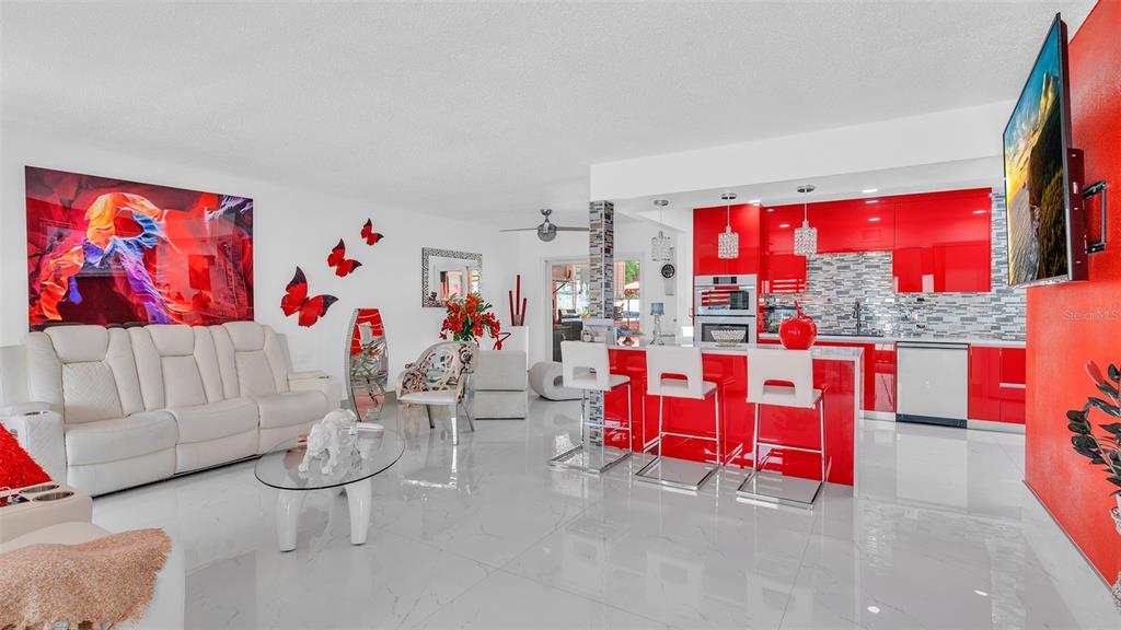 A bright open-concept living room and kitchen featuring white tile floors and vibrant red cabinetry — 8301 LOPEZ DRIVE, TAMPA, FL