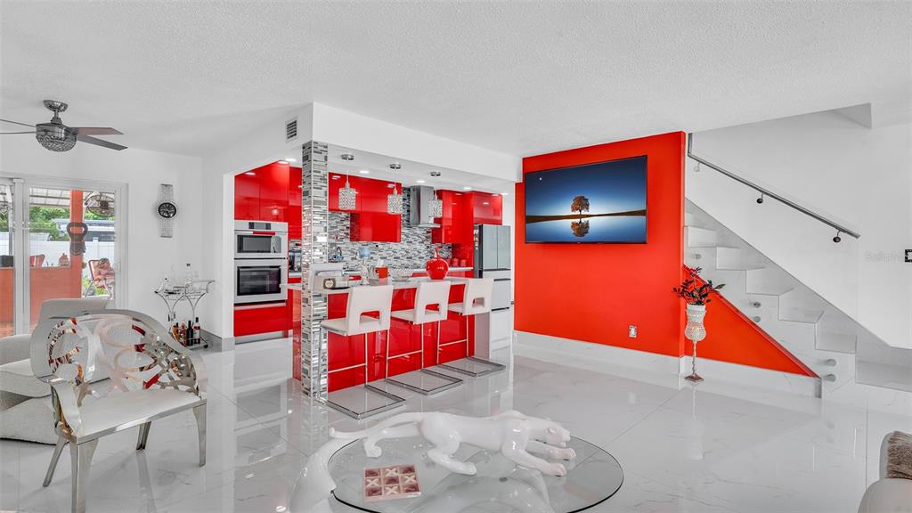 A modern living room and kitchen area features red cabinetry, white tile floors, and a staircase — 8301 LOPEZ DRIVE, TAMPA, FL