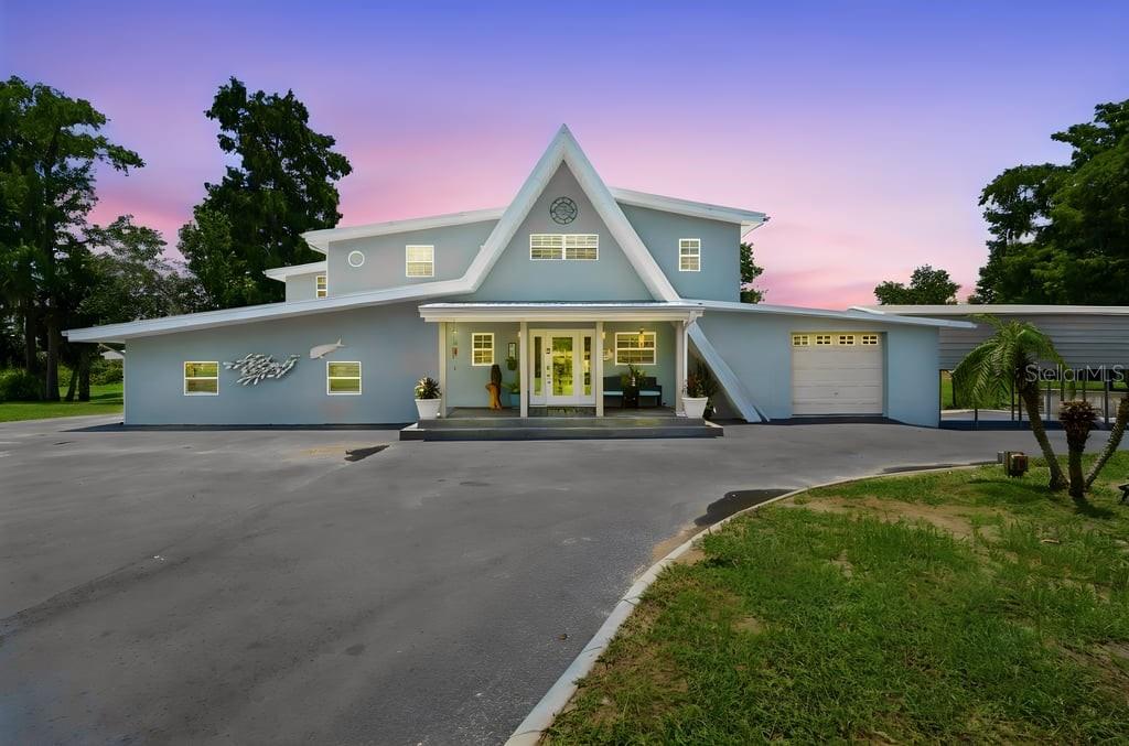 A large, light-green two-story house with a metal roof sits behind a wide asphalt driveway — 220 BRANDY COURT, DELTONA, FL