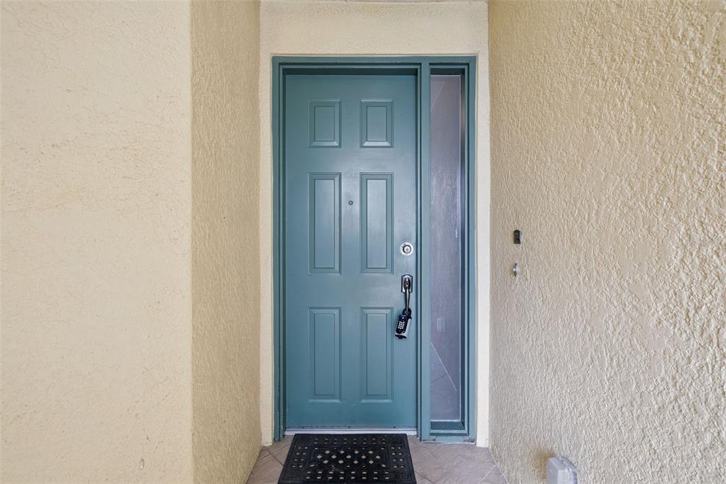 A teal front door with a side window is set within a beige stucco entryway — 8743 THE ESPLANADE UNIT 34, ORLANDO, FL