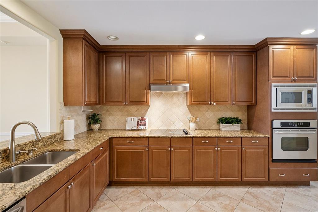 A kitchen features wood cabinets, granite countertops, stainless steel appliances, and a tiled backsplash — 8743 THE ESPLANADE UNIT 34, ORLANDO, FL