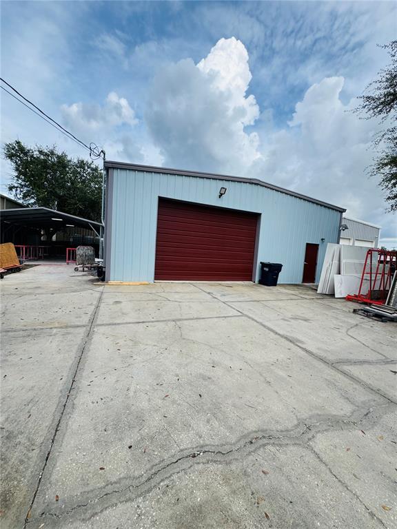 A metal warehouse building with a red roll-up door sits behind a chain-link fence — 4825 N LAUBER WAY, TAMPA, FL