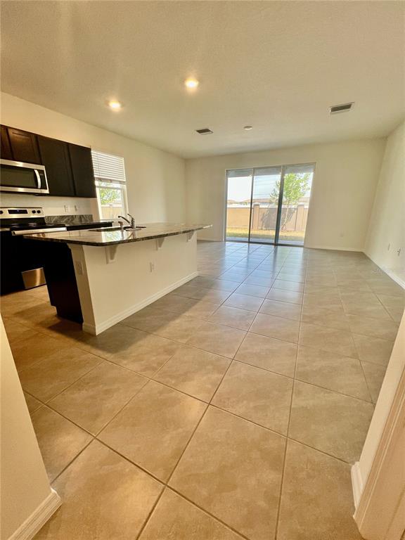 A kitchen with dark cabinets and an island overlooks a tiled living area with sliding doors — 32557 TURTLE GRACE LOOP, WESLEY CHAPEL, FL