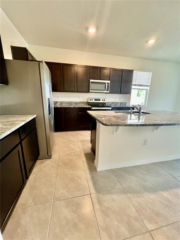 A kitchen features dark wood cabinets, granite countertops, stainless steel appliances, and light tile flooring — 32557 TURTLE GRACE LOOP, WESLEY CHAPEL, FL
