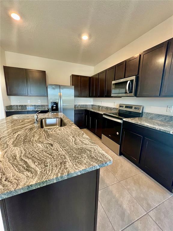 A kitchen features dark wood cabinets, granite countertops, a center island, and stainless steel appliances — 32557 TURTLE GRACE LOOP, WESLEY CHAPEL, FL
