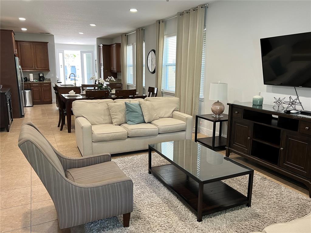 A living room with a beige sofa, striped armchair, glass coffee table, and open-concept kitchen — 370 LASSO DRIVE, KISSIMMEE, FL