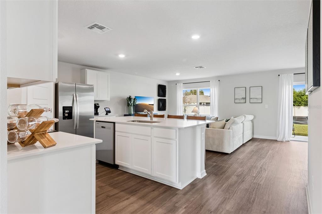 A bright open-concept kitchen and living area with white cabinets, an island, and wood flooring — 1080 BEAR HAMMOCK DRIVE, UMATILLA, FL