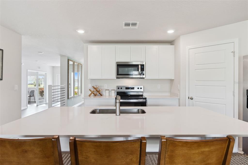 A kitchen features a white quartz island, stainless steel appliances, and white cabinetry — 1080 BEAR HAMMOCK DRIVE, UMATILLA, FL