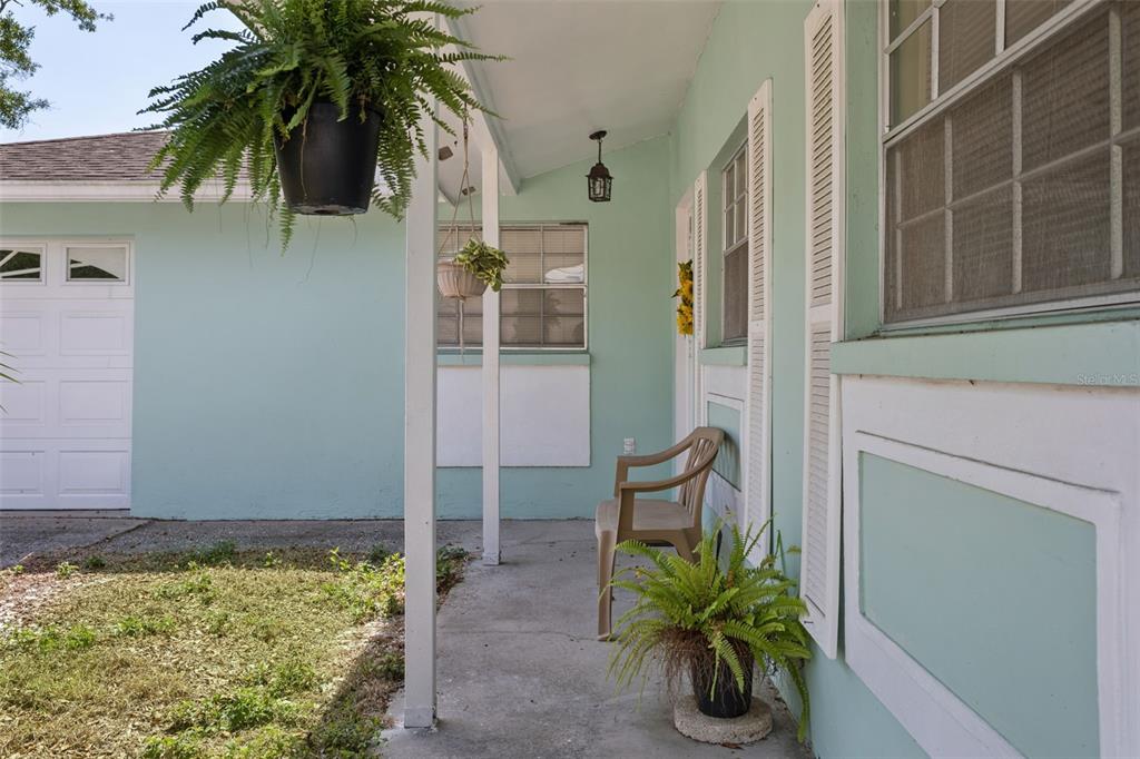 A light green house exterior features a covered concrete porch with a chair and plants — 502 AVOCADO CIRCLE, BRANDON, FL