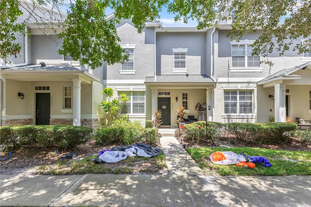 A row of three attached townhouses features gray stucco exteriors, covered front porches, and small lawns — 4620 CAPITAL BOULEVARD, ST CLOUD, FL