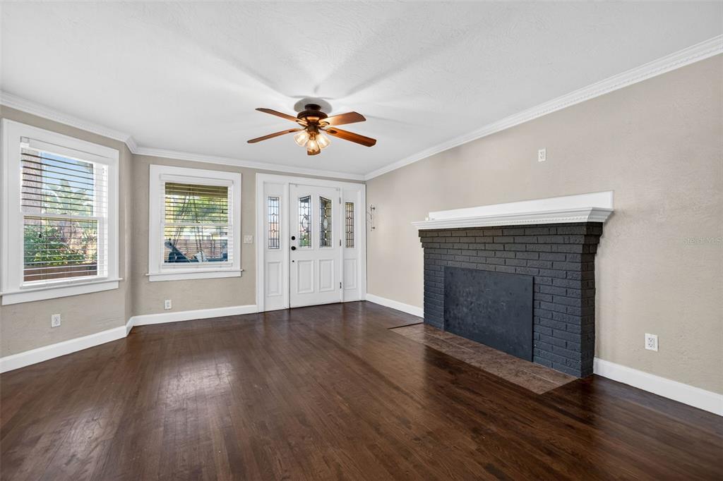 A living room with dark wood floors, a brick fireplace, and a white front door — 2419 DARTMOUTH AVENUE N, ST PETERSBURG, FL