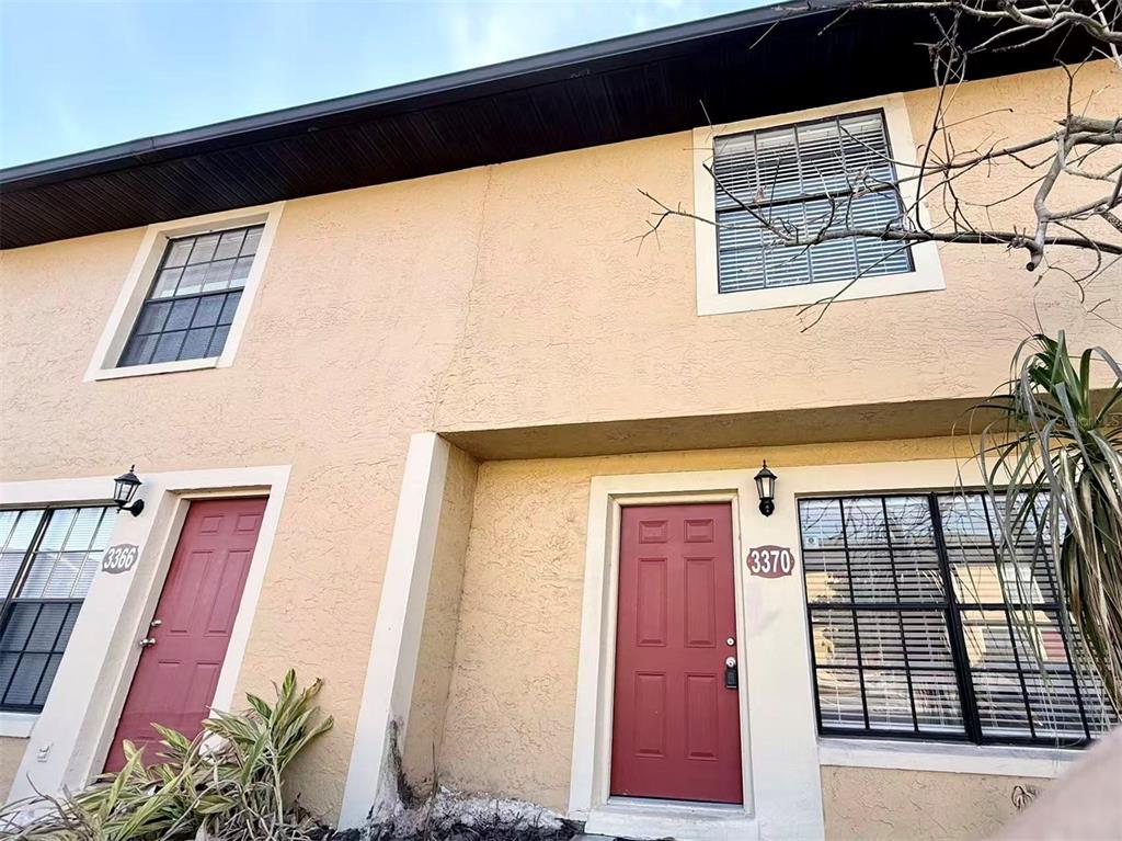 The exterior of a two-story stucco townhouse features two red doors and dark-framed windows — 3370 CEDAR SPRINGS PLACE UNIT 156, WINTER PARK, FL