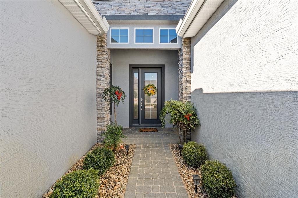 A paved walkway leads to a front door framed by stone pillars and landscaping — 831 PINEWOOD DRIVE, ORMOND BEACH, FL