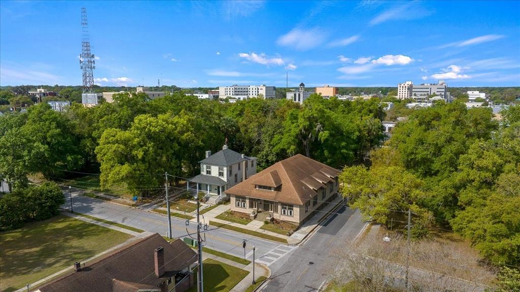 An aerial view shows two adjacent buildings surrounded by trees near a city skyline — 118 NE TUSCAWILLA AVENUE, OCALA, FL