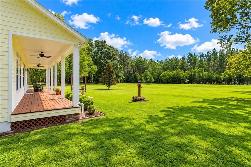 A yellow house with a covered wooden porch overlooks a large, grassy backyard with trees — 2451 NE 120TH STREET, CHIEFLAND, FL