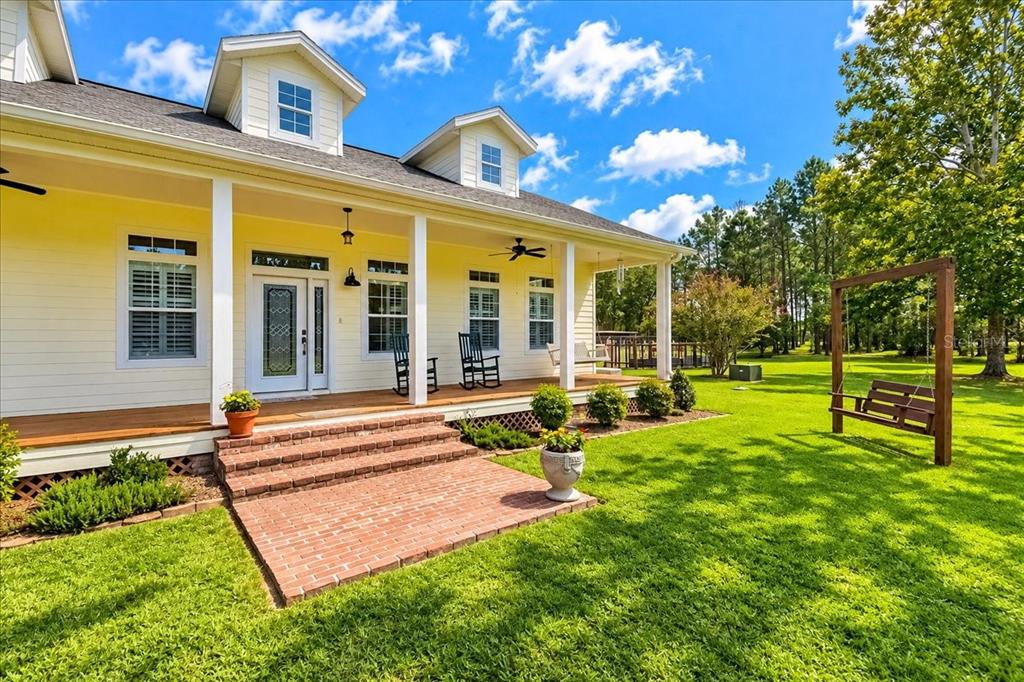 A yellow house with a covered porch, brick steps, and a wooden swing in the yard — 2451 NE 120TH STREET, CHIEFLAND, FL