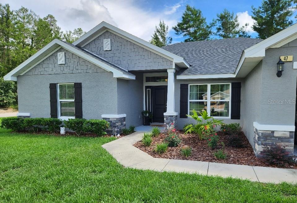 A gray single-story house features a shingled gable, black shutters, and a covered front entryway — 47 VILLAGE CENTER DRIVE, HOMOSASSA, FL