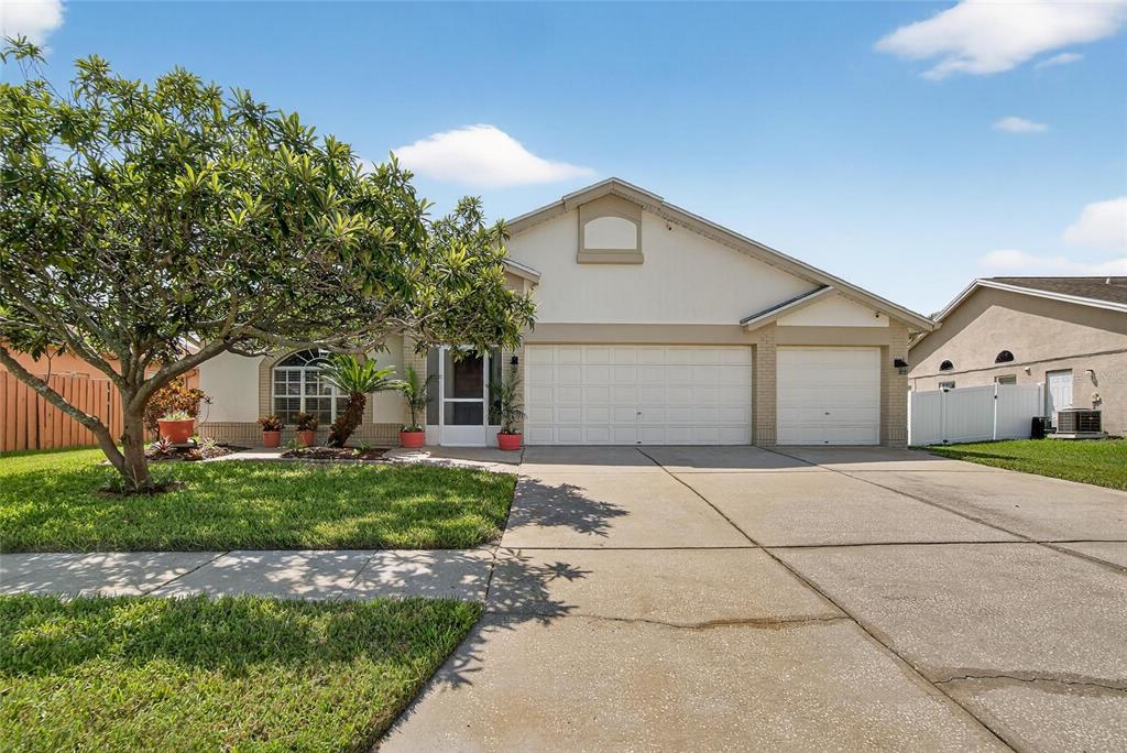 A single-story house with a beige stucco exterior, a three-car garage, and a front lawn — 13029 PRESTWICK DRIVE, RIVERVIEW, FL