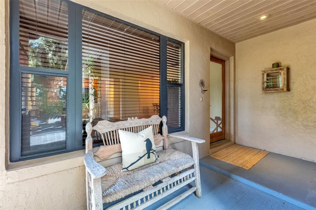 A covered porch features a wooden bench with a bird-patterned pillow and a glass-paneled door — 1850 BRYAN AVENUE, WINTER PARK, FL