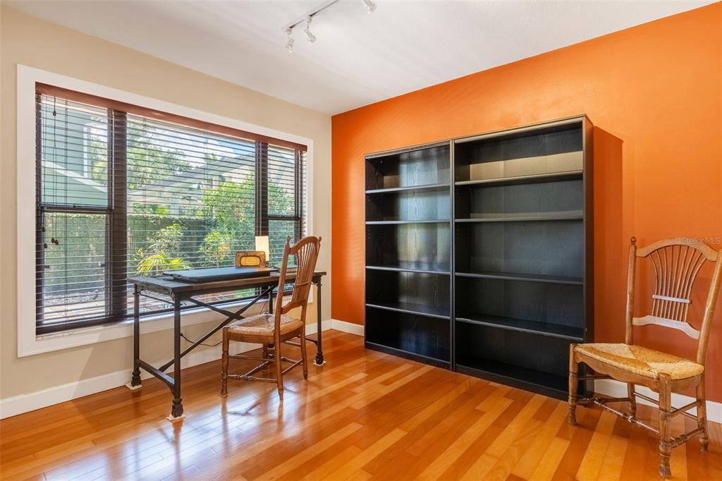 A home office features orange walls, hardwood floors, a desk by the window, and bookshelves — 1850 BRYAN AVENUE, WINTER PARK, FL