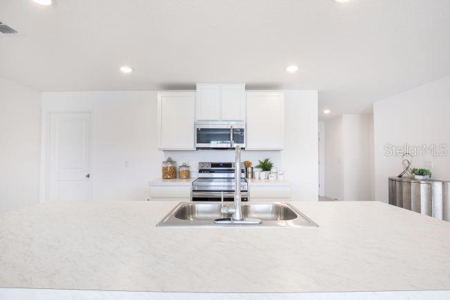 A modern kitchen features white cabinets, stainless steel appliances, and a large central island — 16077 MALDEN ROAD, WEEKI WACHEE, FL
