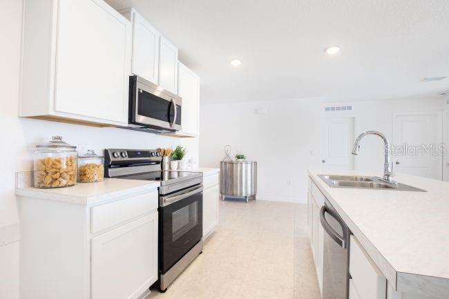 A modern kitchen features white cabinets, stainless steel appliances, and a central island with sink — 16077 MALDEN ROAD, WEEKI WACHEE, FL