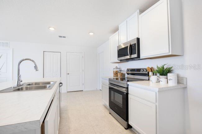 A kitchen features white cabinets, stainless steel appliances, and a sink on a laminate countertop — 16077 MALDEN ROAD, WEEKI WACHEE, FL