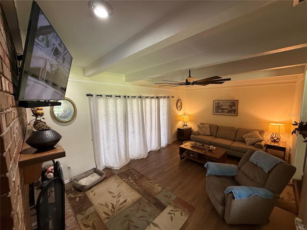 A living room features a brick fireplace, wood-look flooring, a ceiling fan, and sliding doors — 305 WHITE OAK DRIVE, ALTAMONTE SPRINGS, FL