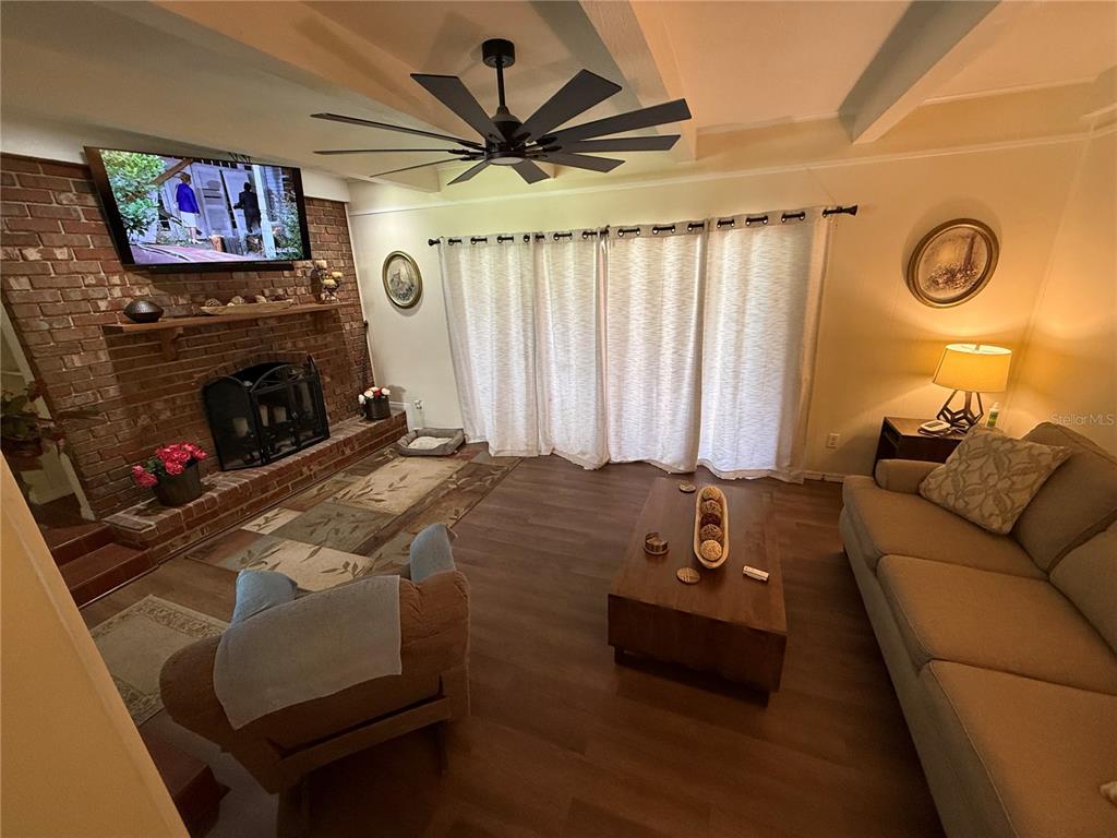 A living room features a brick fireplace, wood-look flooring, a ceiling fan, and sliding doors — 305 WHITE OAK DRIVE, ALTAMONTE SPRINGS, FL