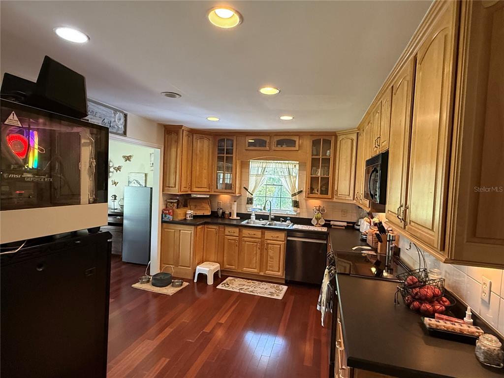 A kitchen features wood cabinets, black countertops, stainless steel appliances, and hardwood flooring — 305 WHITE OAK DRIVE, ALTAMONTE SPRINGS, FL