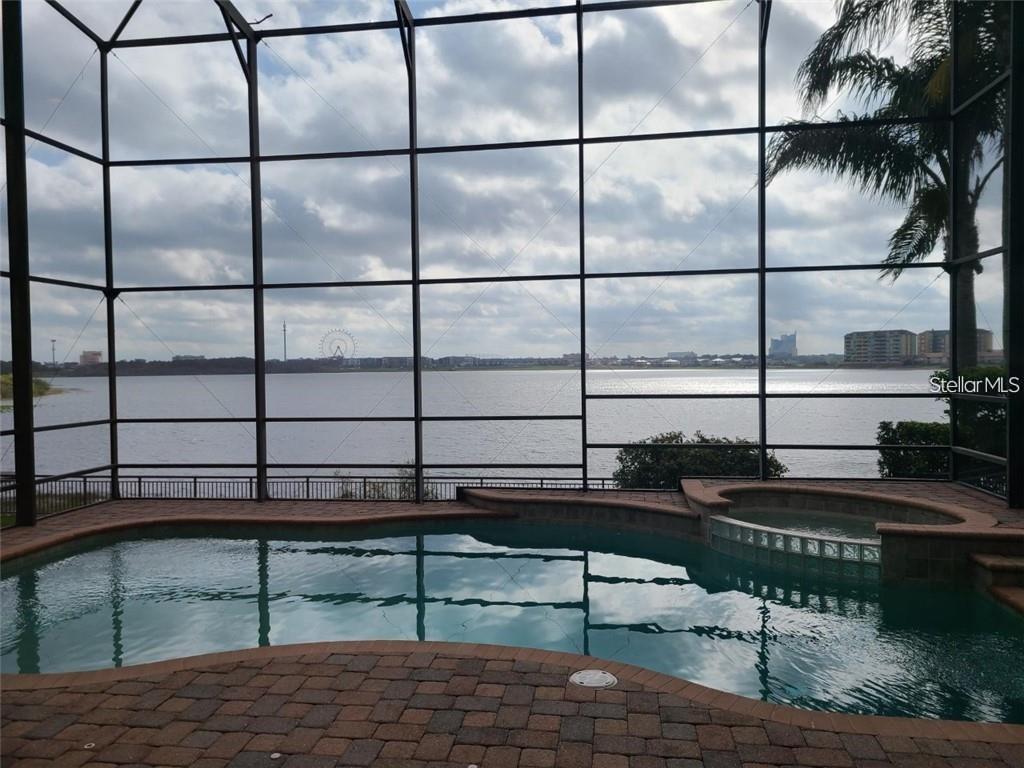 A screened-in pool and spa overlook a large lake with a distant Ferris wheel — 8149 VIA ROSA, ORLANDO, FL
