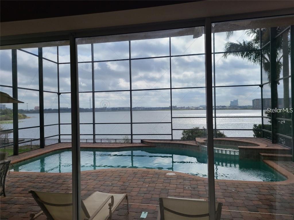 A screened-in pool patio overlooks a lake with a distant Ferris wheel and city skyline — 8149 VIA ROSA, ORLANDO, FL