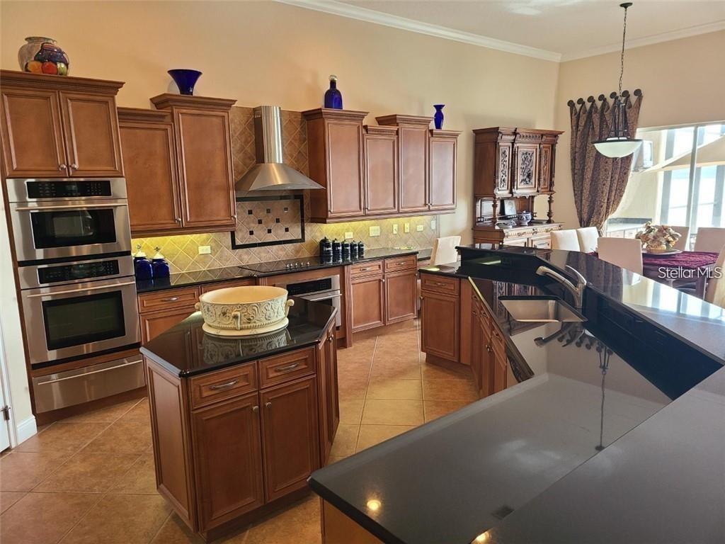 A kitchen features wood cabinets, black countertops, stainless steel appliances, and tile flooring — 8149 VIA ROSA, ORLANDO, FL