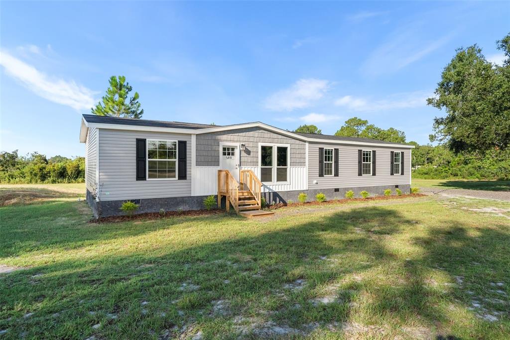 A single-story manufactured home with gray siding, a small wooden porch, and black shutters — 12610 SE 115 STREET, OCKLAWAHA, FL