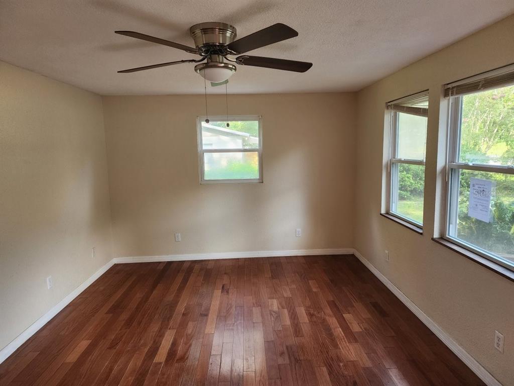 An empty room features hardwood floors, a ceiling fan, and windows with natural light — 2861 SE 18TH AVENUE, GAINESVILLE, FL