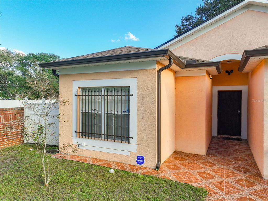The exterior of a peach-colored house features a window with security bars and tiled flooring — 4687 WESTGROVE WAY, ORLANDO, FL