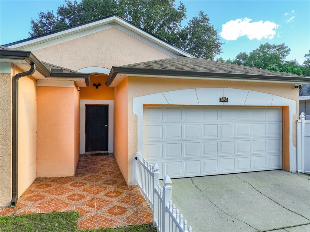 A peach-colored house exterior features a white garage door, a tiled entryway, and a white fence — 4687 WESTGROVE WAY, ORLANDO, FL