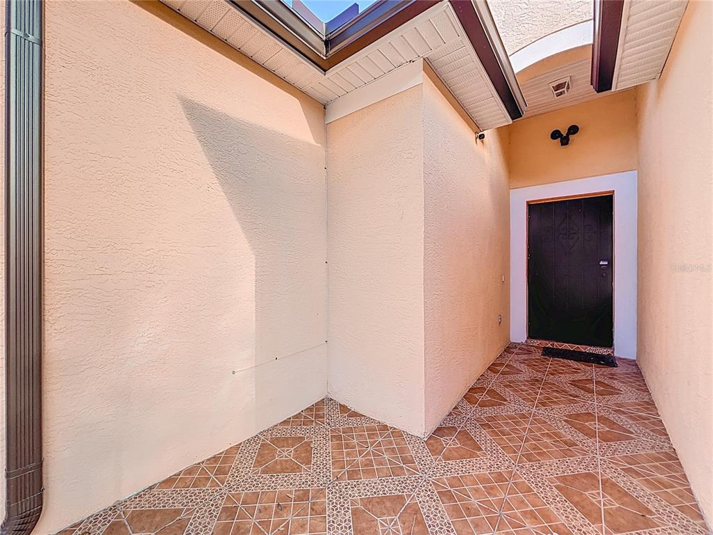 An exterior entryway features a dark door, peach-colored stucco walls, and patterned tile flooring — 4687 WESTGROVE WAY, ORLANDO, FL