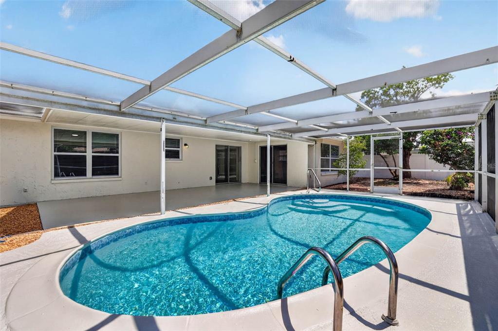 A swimming pool with a metal ladder sits inside a screened-in patio enclosure — 7604 JASMINE BOULEVARD, PORT RICHEY, FL