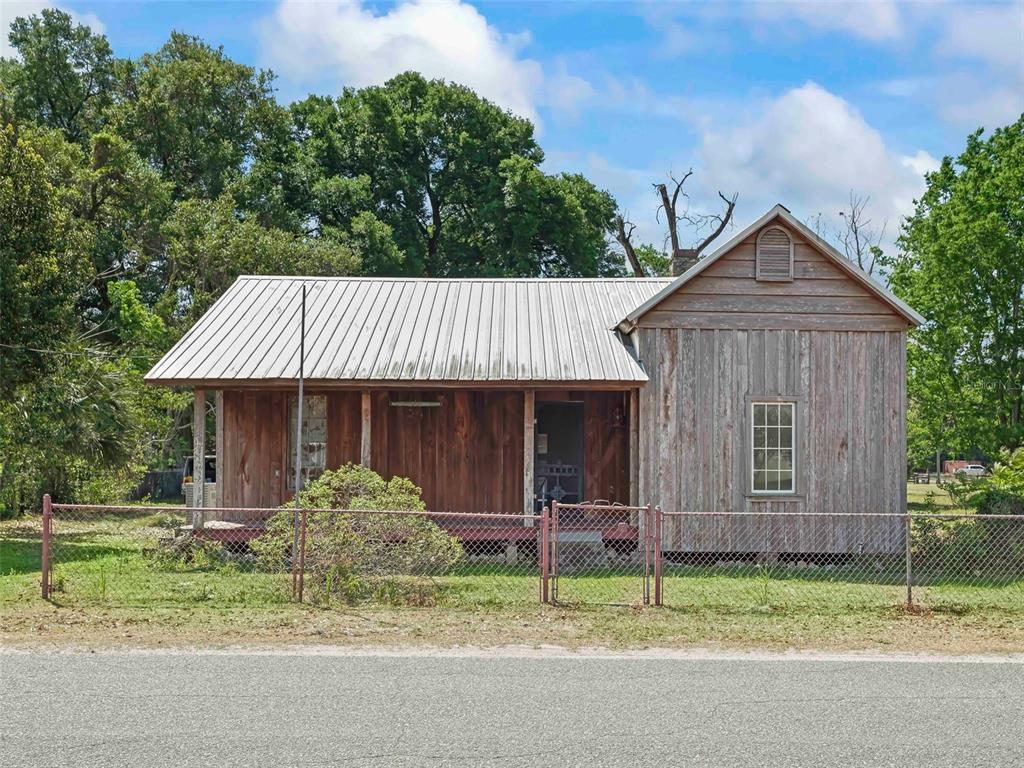 A weathered wooden house with a metal roof sits behind a chain-link fence — 4241 COUNTY ROAD 106, OXFORD, FL