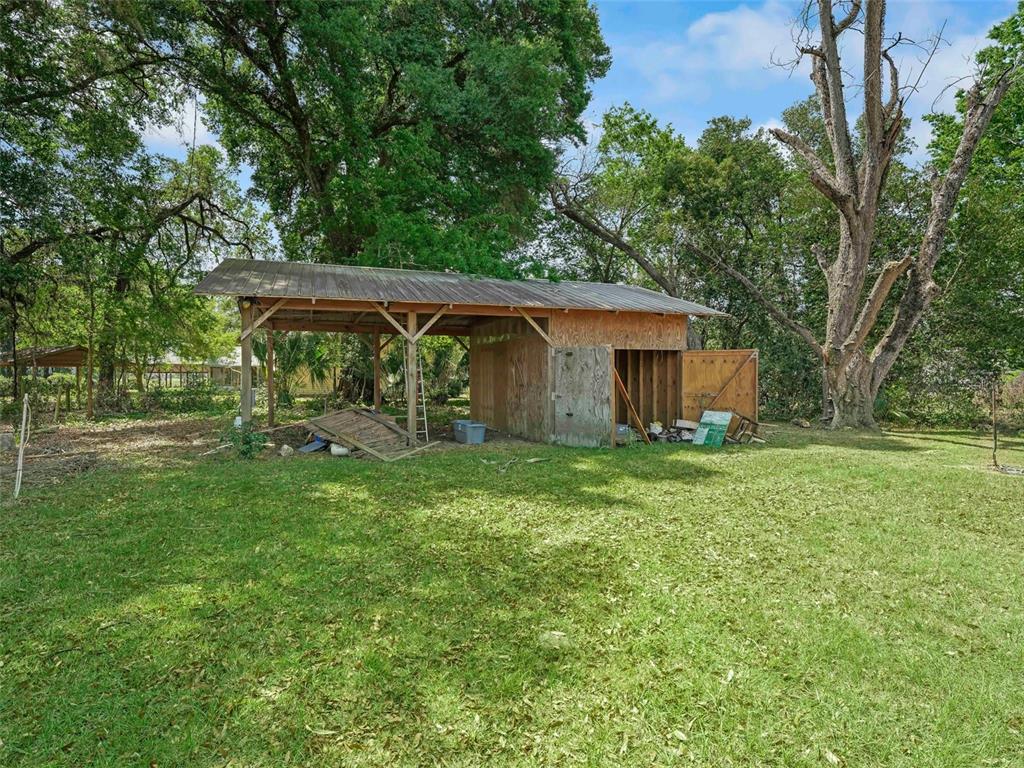 A wooden shed with an attached open-sided carport sits in a grassy, tree-filled yard — 4241 COUNTY ROAD 106, OXFORD, FL
