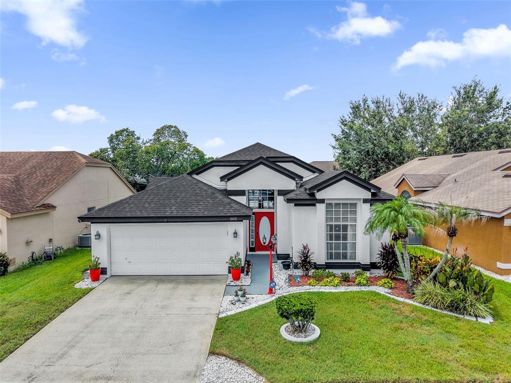 A single-story house with a white stucco exterior, dark roof, and a red front door — 502 BRIGHTVIEW DRIVE, LAKE MARY, FL