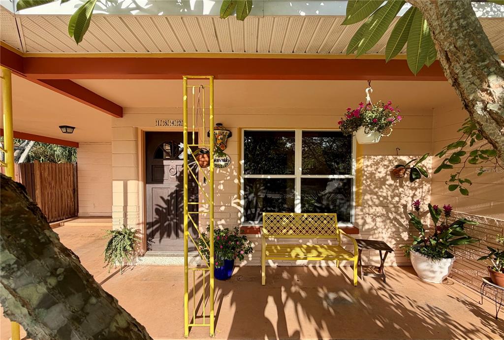 A covered front porch features a yellow bench, potted plants, and a dark wooden door — 1842 59TH STREET S, GULFPORT, FL