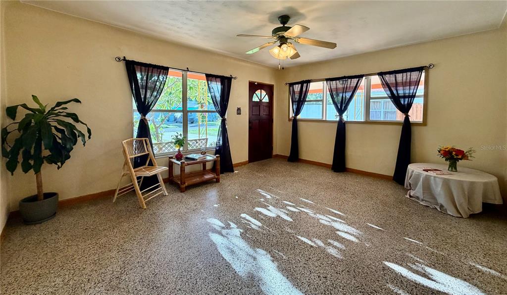 A living room with beige walls, a speckled floor, a ceiling fan, and large windows — 1842 59TH STREET S, GULFPORT, FL