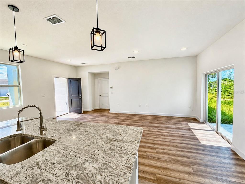 A kitchen island with a granite countertop overlooks an open living area with wood-look flooring — 424 MAITLAND COURT, POINCIANA, FL