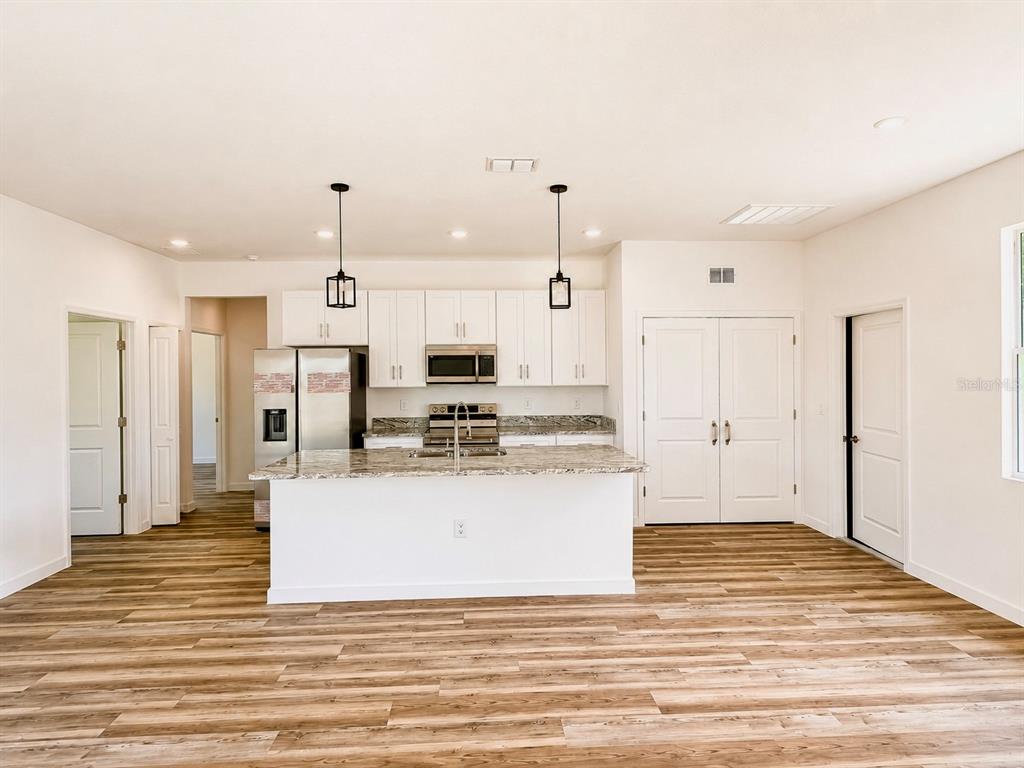 A kitchen features white cabinets, granite countertops, a center island, and wood-look flooring — 424 MAITLAND COURT, POINCIANA, FL