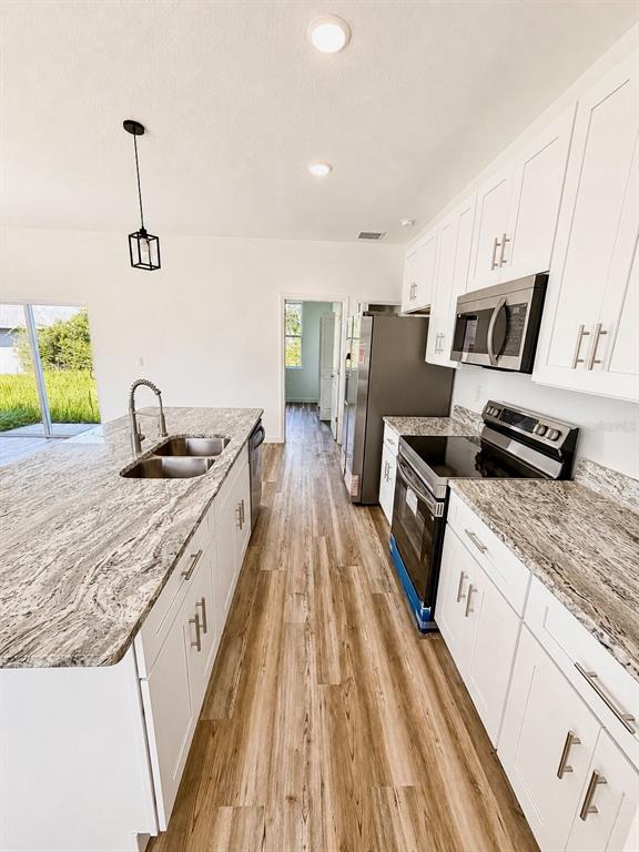 A kitchen features white cabinets, granite countertops, stainless steel appliances, and wood-look flooring — 424 MAITLAND COURT, POINCIANA, FL
