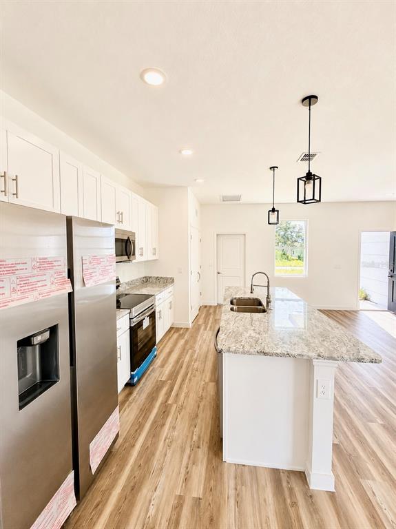 A modern kitchen features white cabinets, granite countertops, stainless steel appliances, and wood-look flooring — 424 MAITLAND COURT, POINCIANA, FL